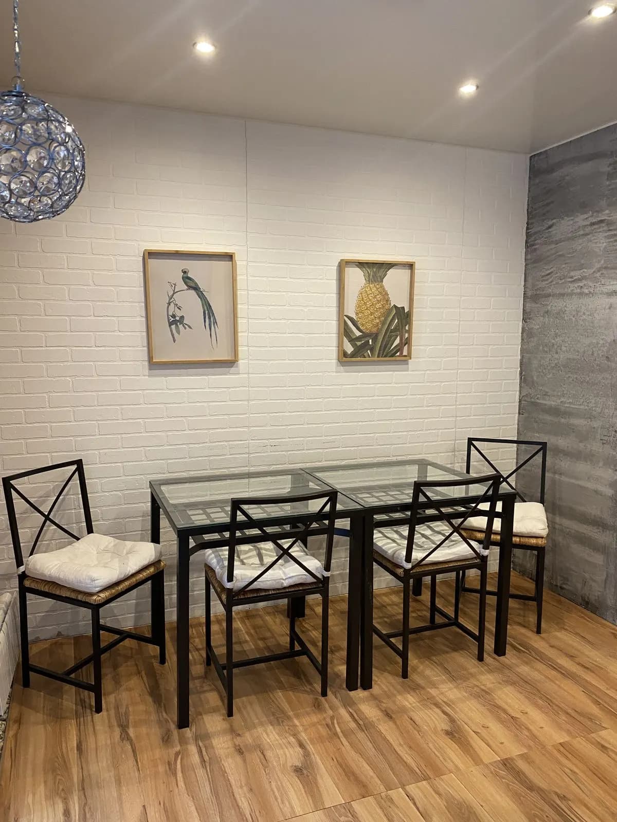 Dining nook with black metal chairs, a glass table, and framed prints on a white brick-texture wall