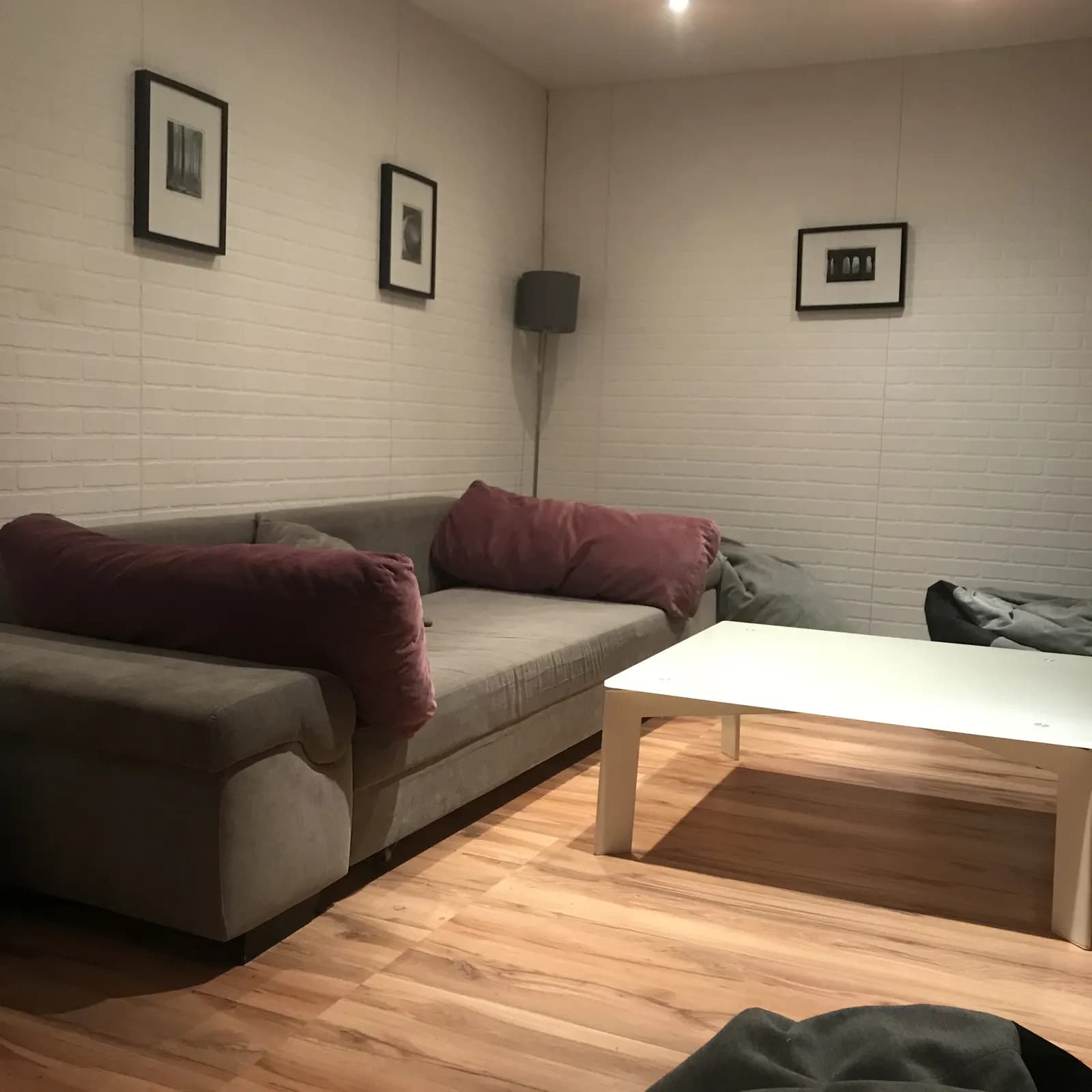 Lounge with a grey sofa, plum cushions, white coffee table, and framed prints on white brick