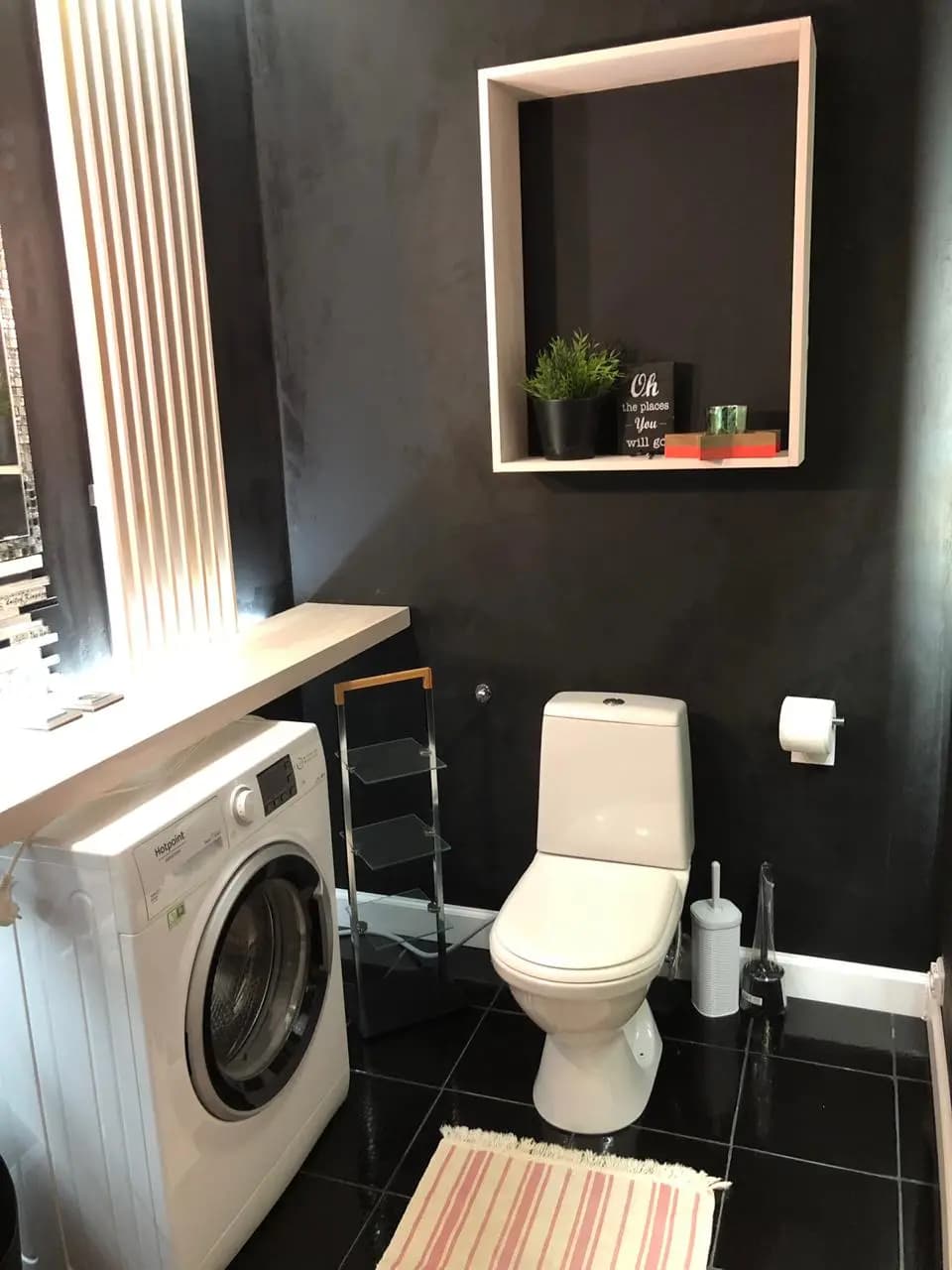 Black bathroom with the washer beside the toilet and a lit display niche above
