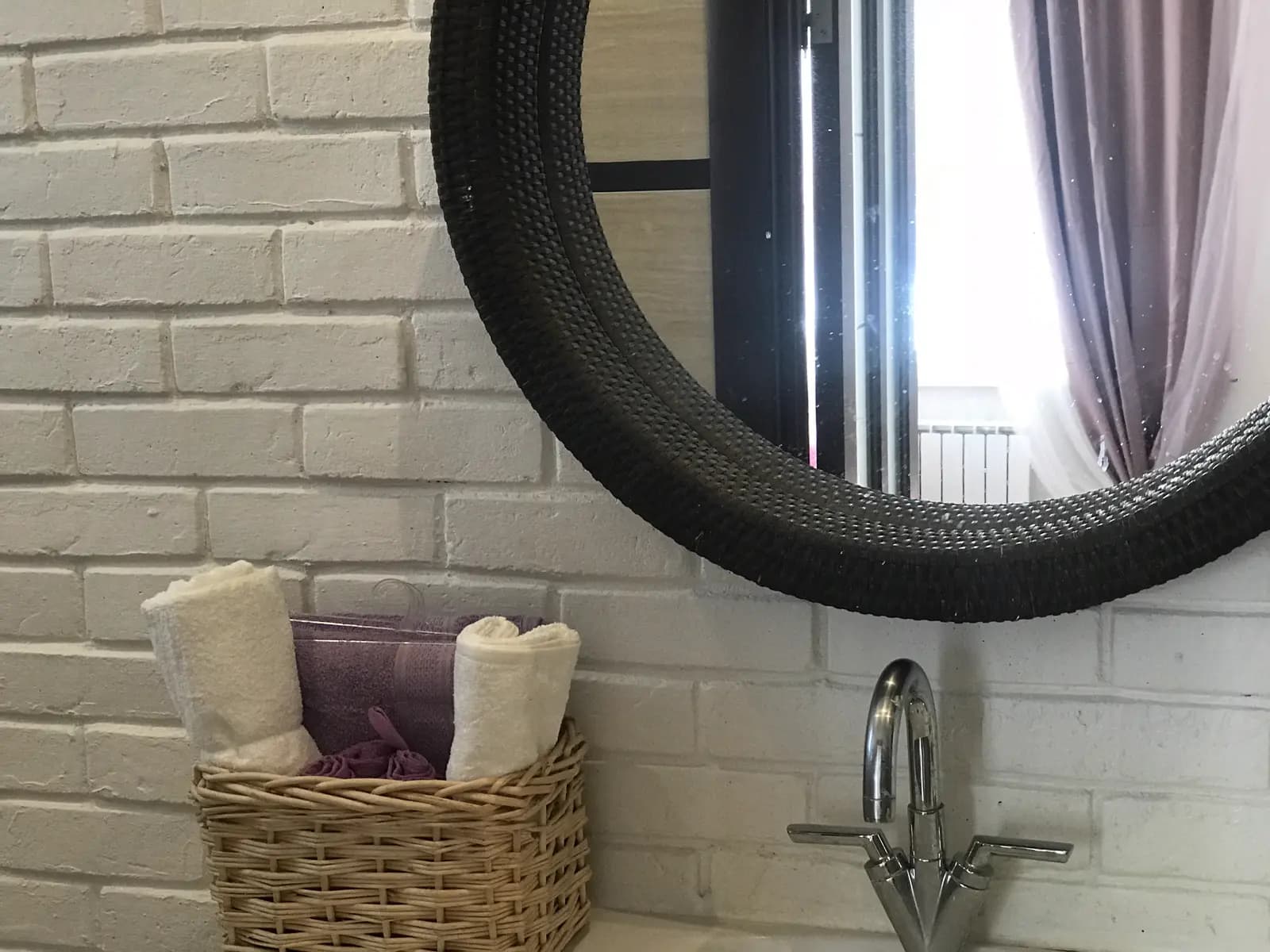 White brick bathroom with a round black-framed mirror and a basket of towels
