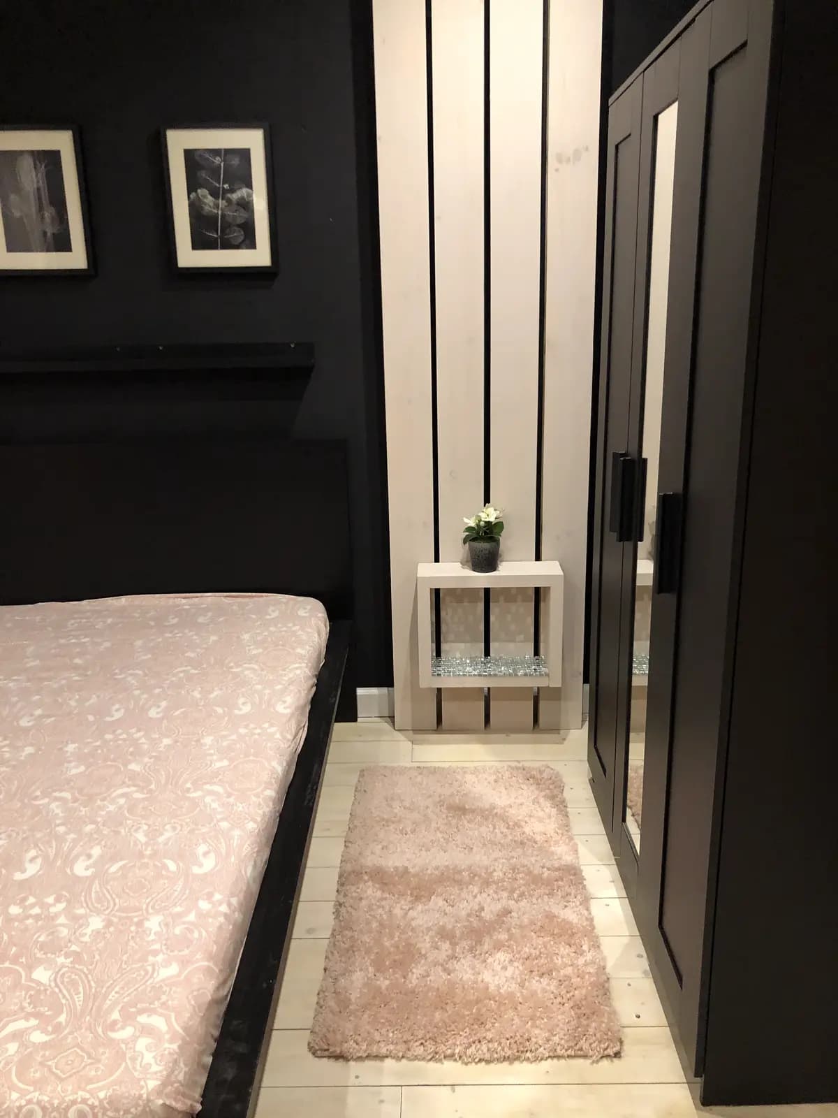 Bedroom with a black upholstered bed, blush rug, and panelled charcoal wall