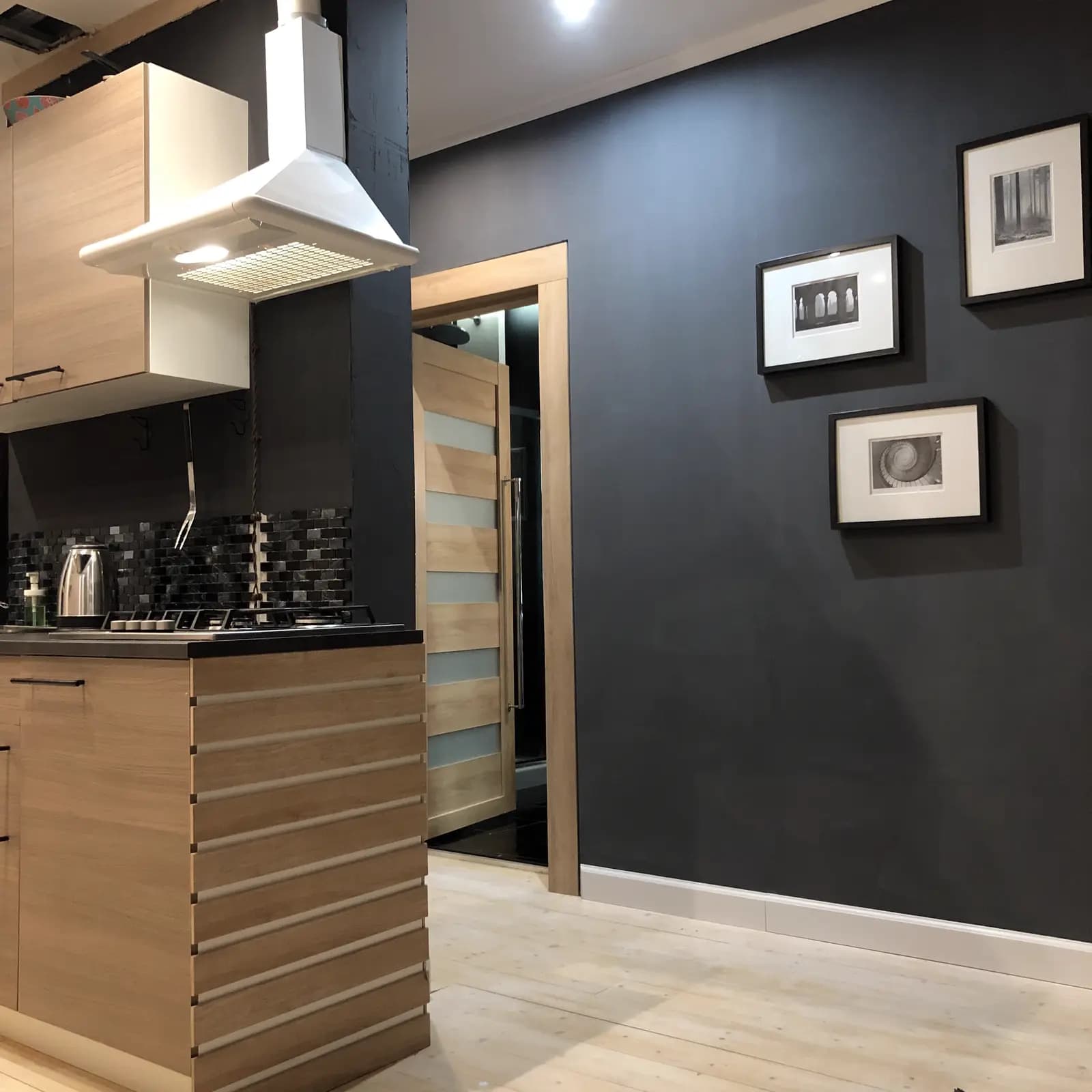 Kitchen island and white hood against charcoal walls with framed monochrome prints