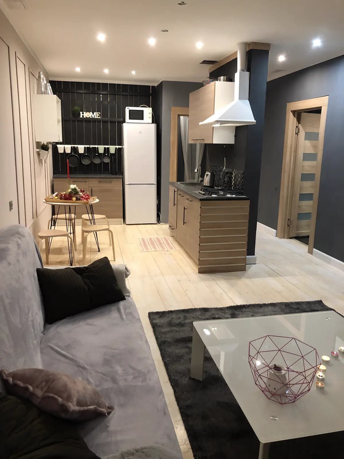 Open kitchen with a wood island, black feature wall, white cabinets, and a small breakfast table
