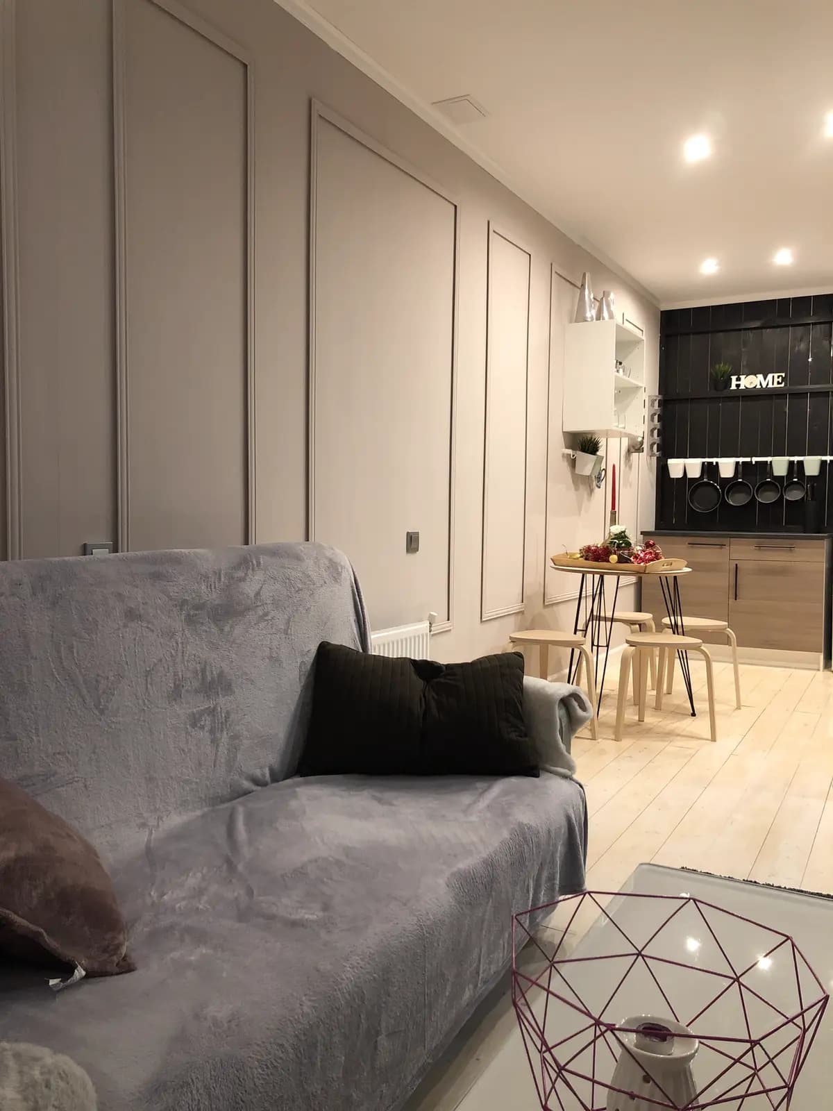 Living area with a grey sofa and panelled charcoal wall opening toward the kitchen