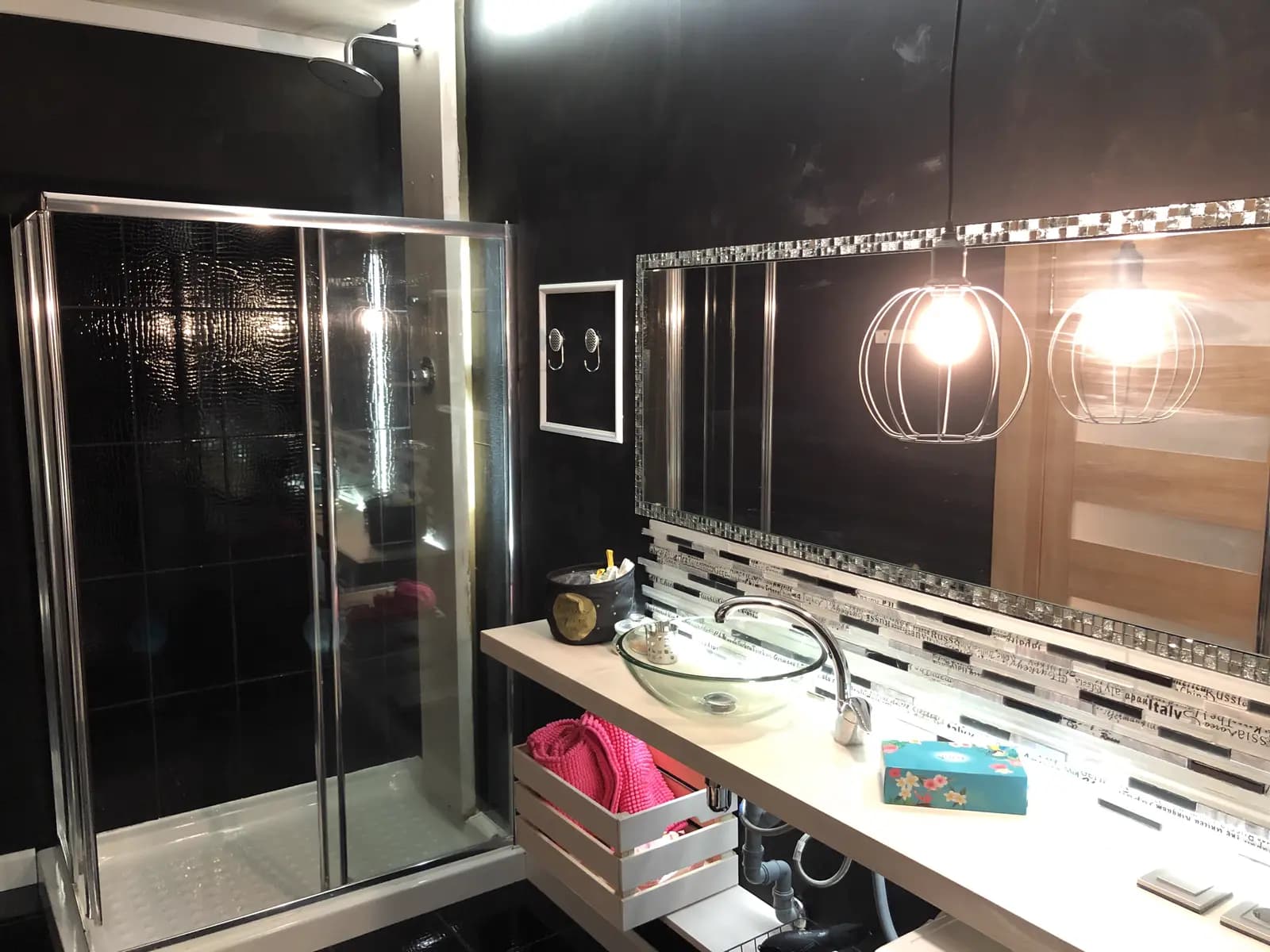 Black-tiled shower room with a caged pendant light, vessel sink, and mosaic ledge