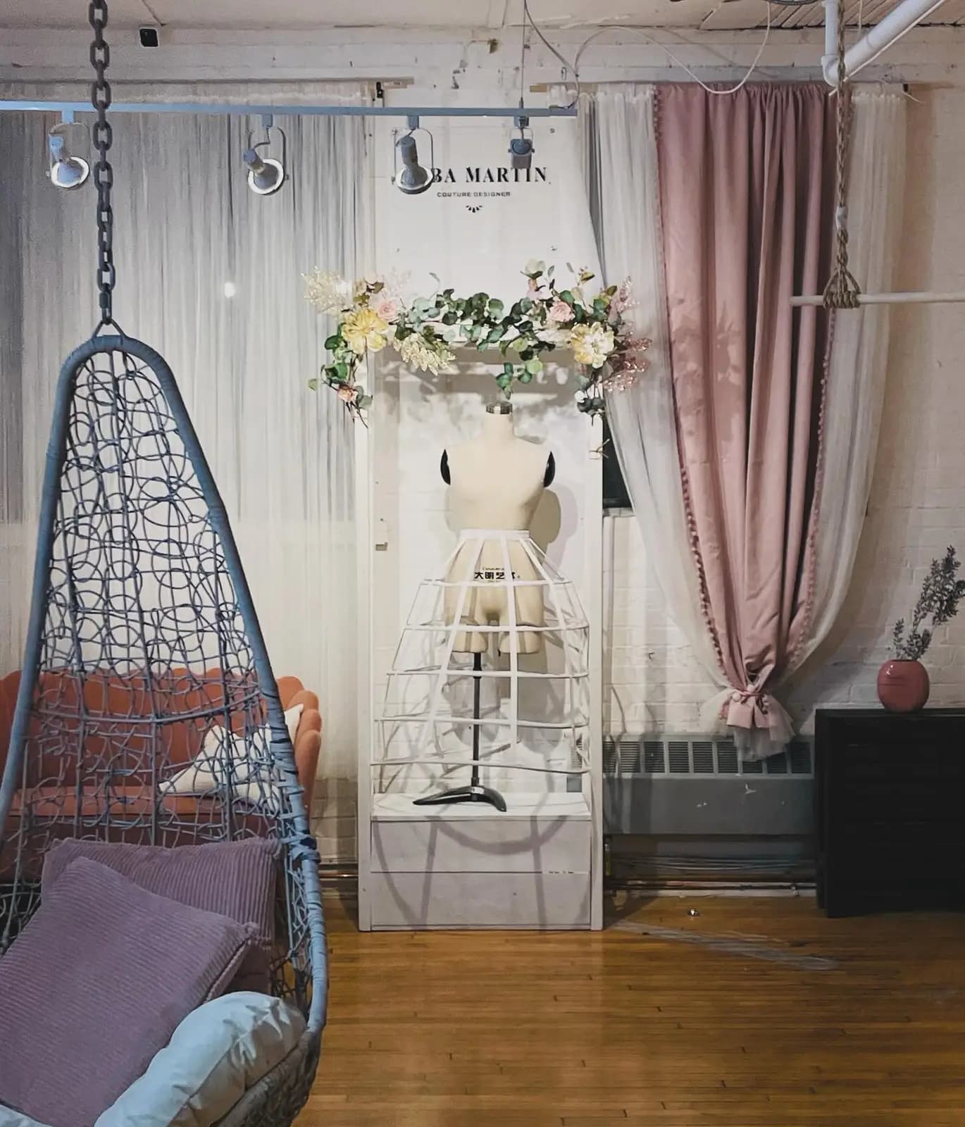 Bridal boutique corner with a hanging rattan chair, blush drapery, and a styled dress-form display