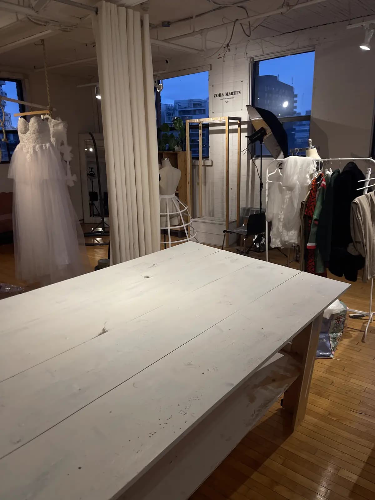 Gowns hung along the window at dusk beside the atelier work table