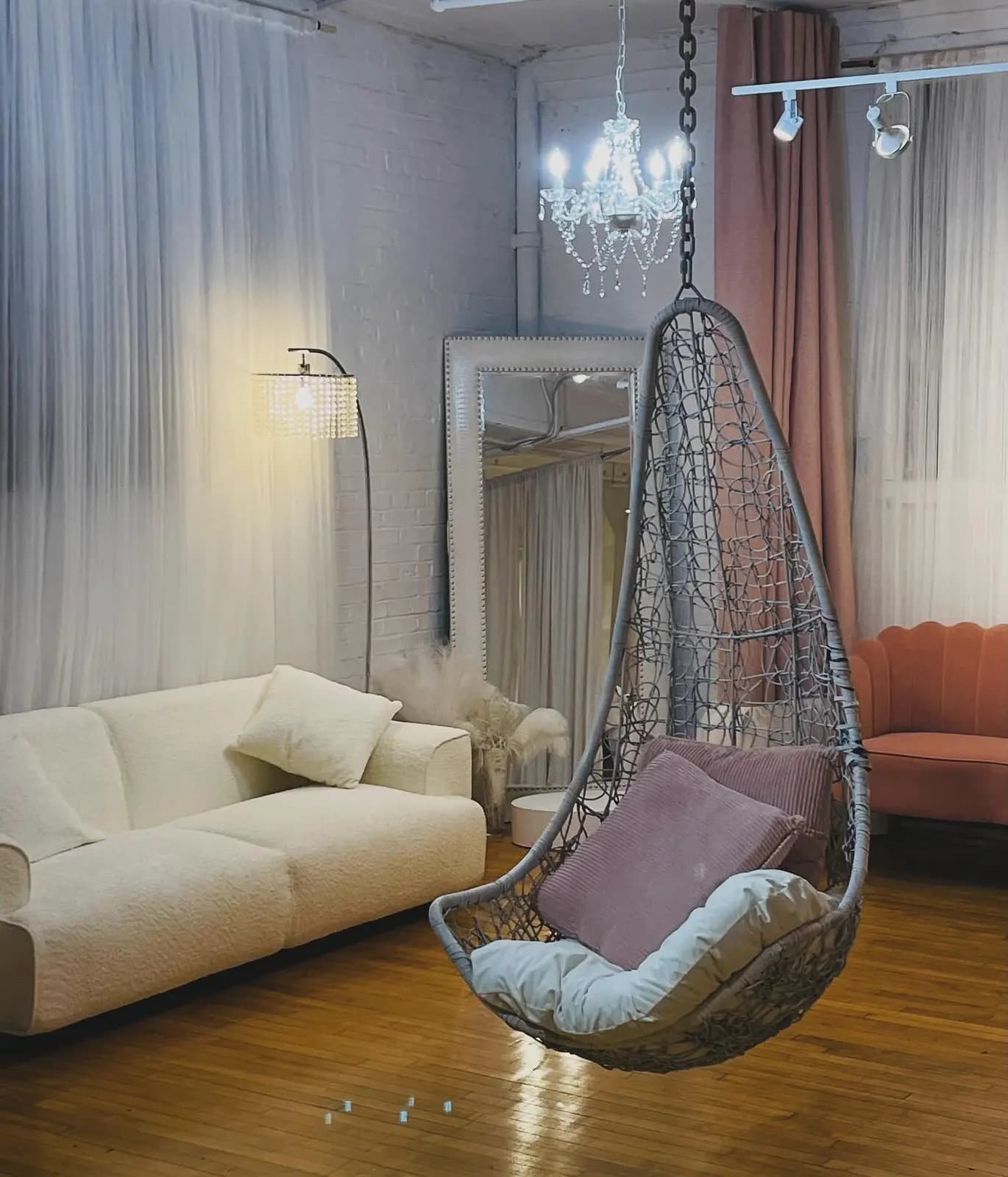 Guest lounge with a cream sofa, hanging chair, chandelier, and full-height mirror