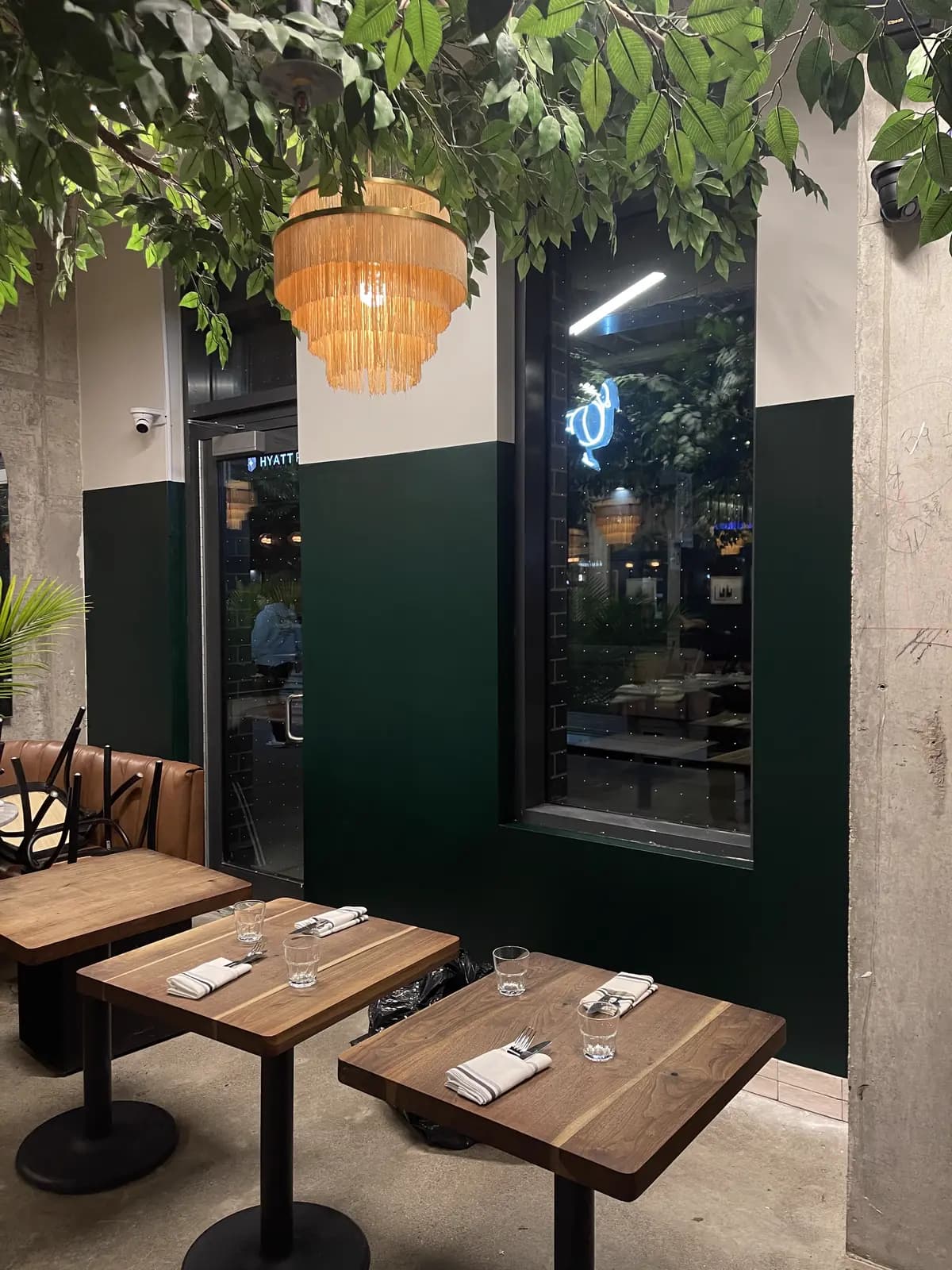 Deep-green café walls in the evening with set tables and a fringed pendant light