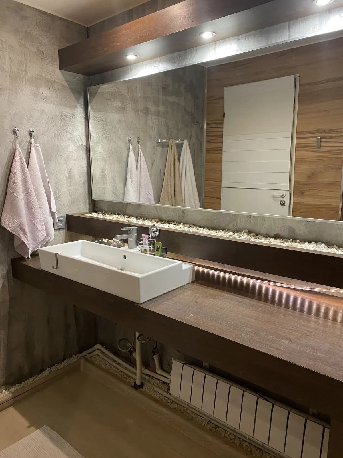 Floating walnut vanity with a white vessel sink, underlit counter, and full-width mirror