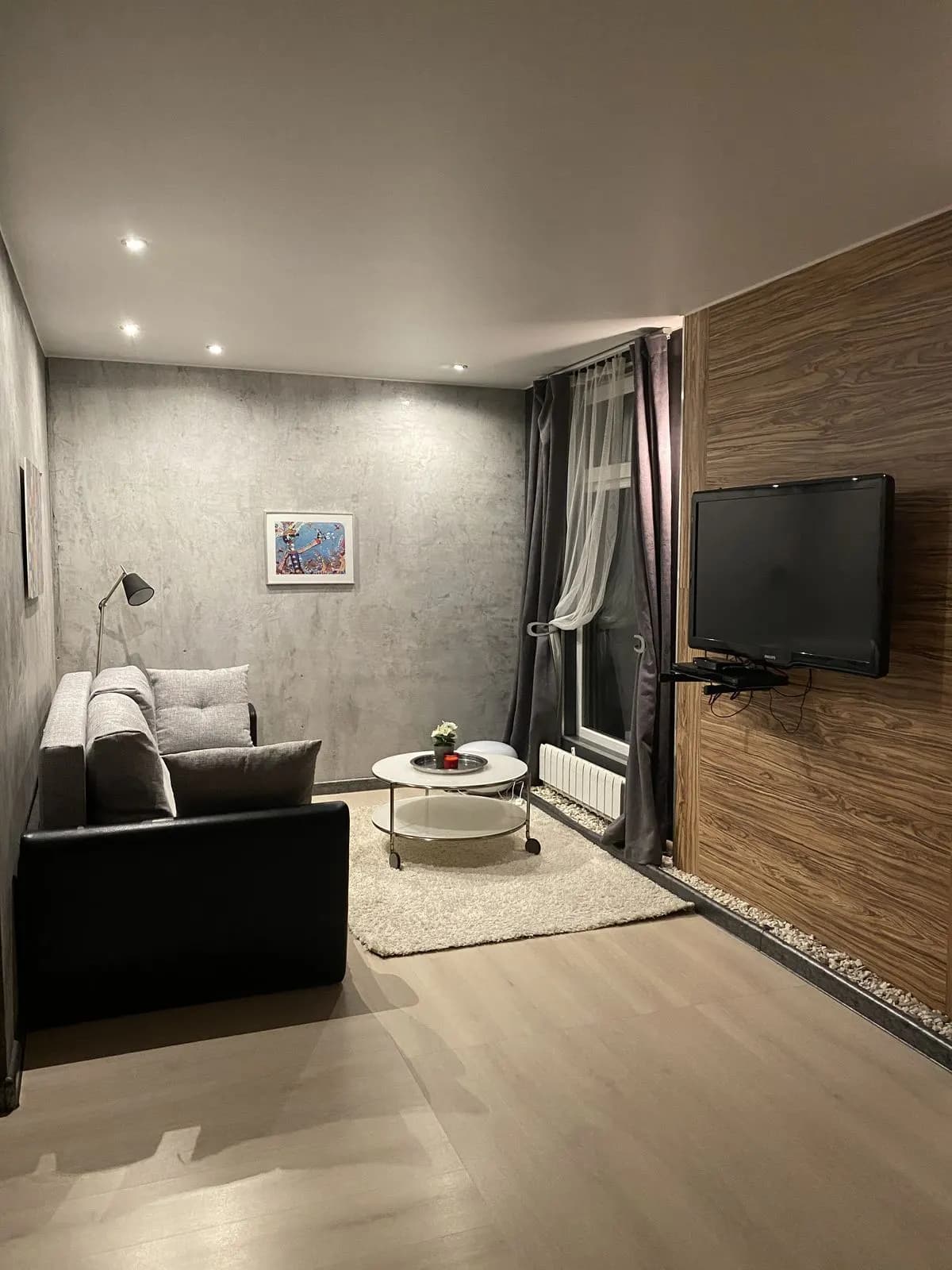 Lounge with a grey sofa, concrete-texture wall, wall-mounted TV, and soft rug