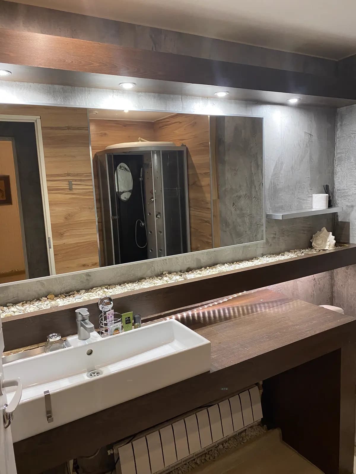 Full-width mirror above the underlit walnut counter with the shower cabin reflected