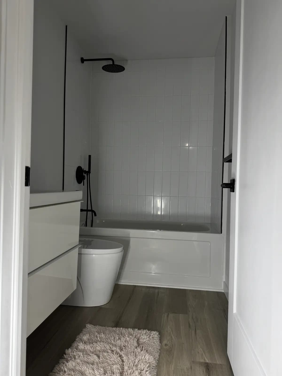 White tub with a matte-black rain shower and glossy subway-tile surround