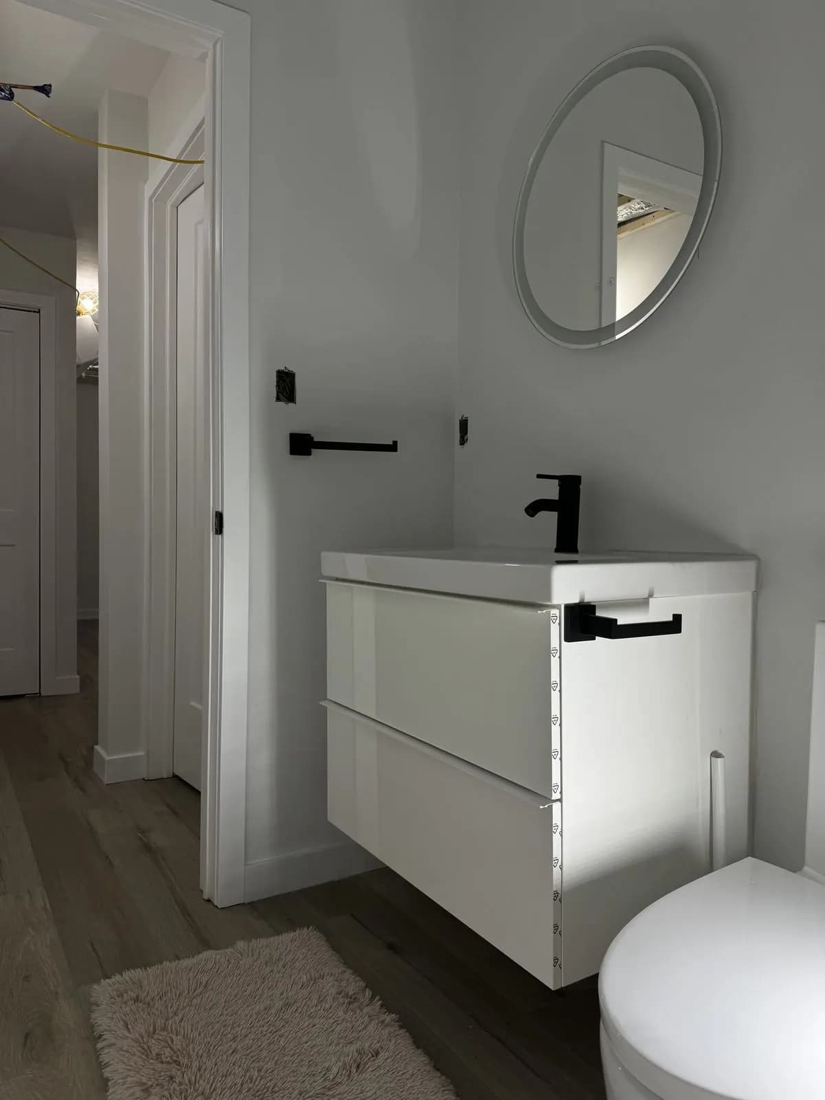Floating white vanity with a matte-black faucet, round mirror, and towel bar