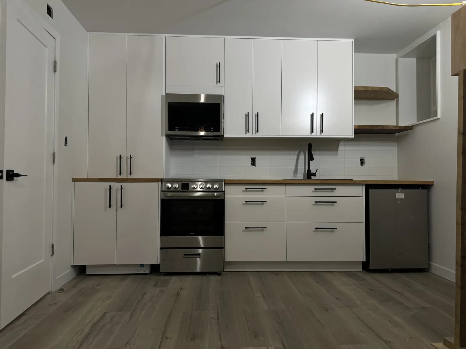 Finished white kitchen with butcher block counters and black fixtures