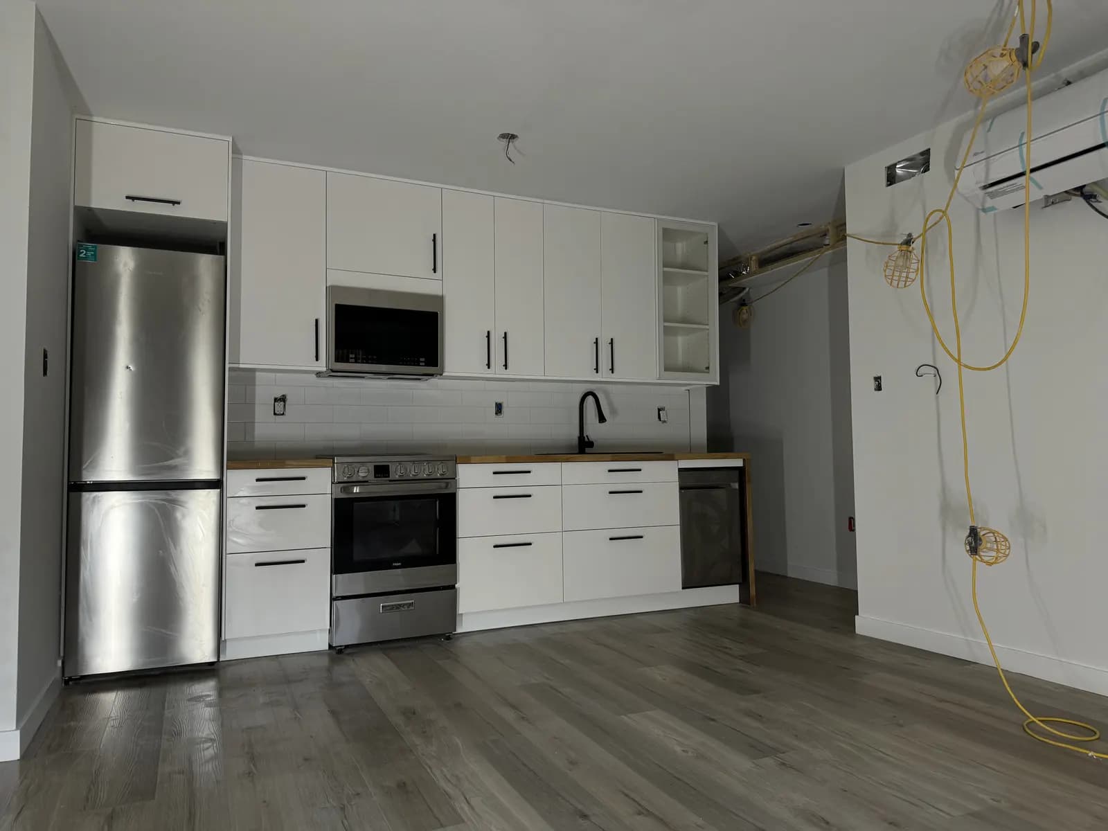 Kitchen mid-renovation with exposed wiring, unfinished walls, and appliances staged in place