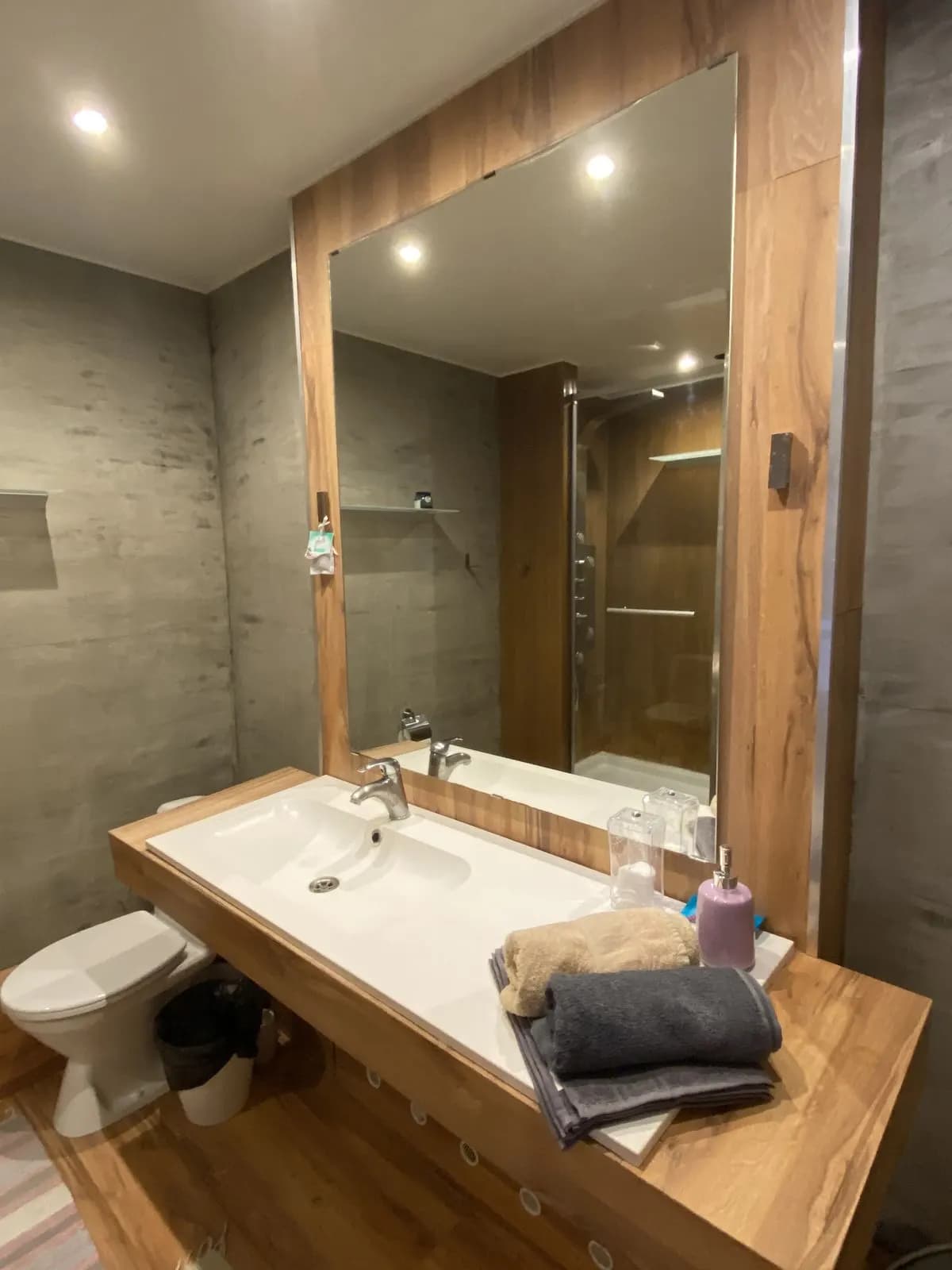 Bathroom vanity with a walnut counter, wide mirror, and warm downlighting