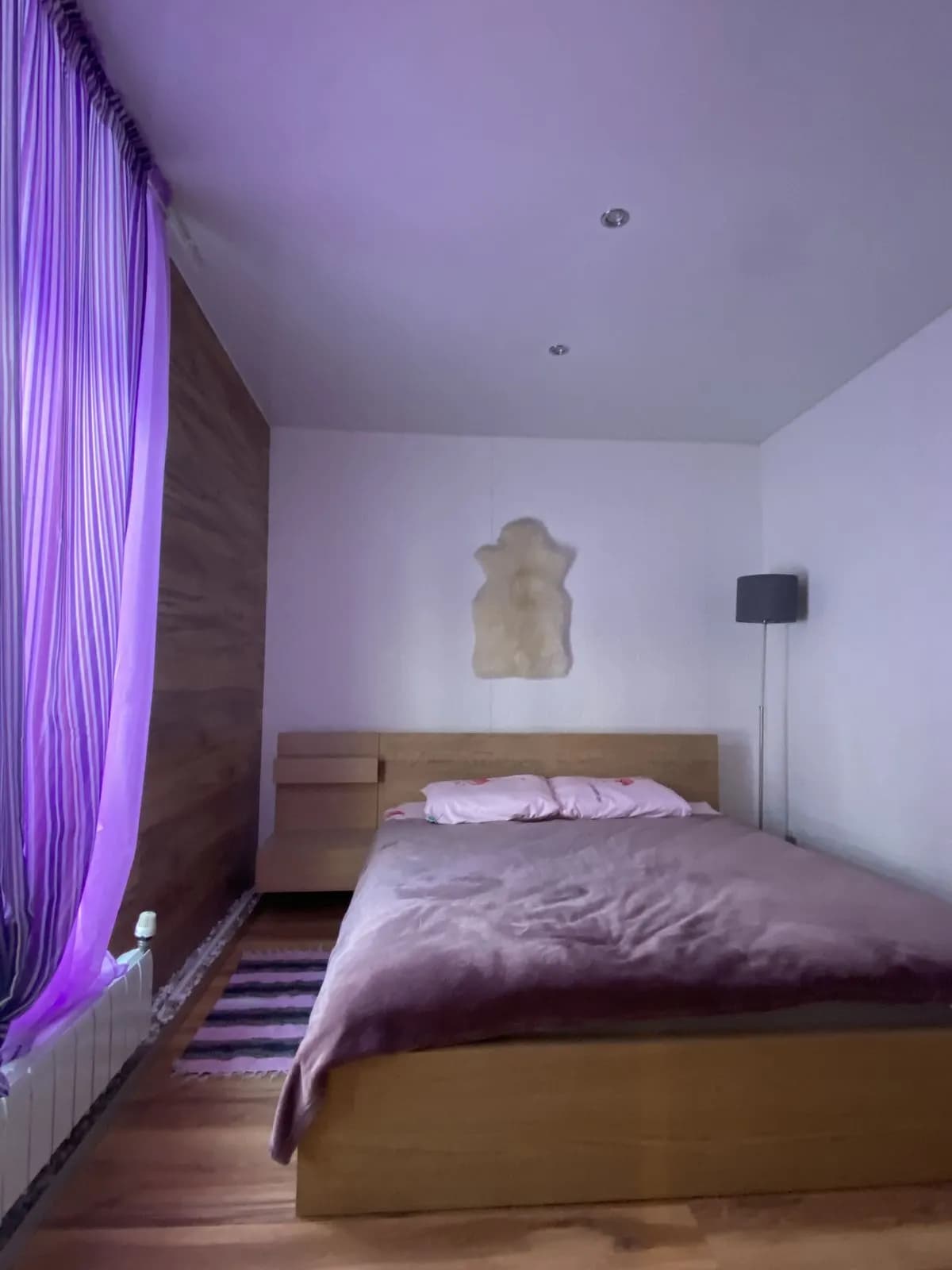 Bedroom with a plum duvet, oak bed frame, and sheer violet curtains