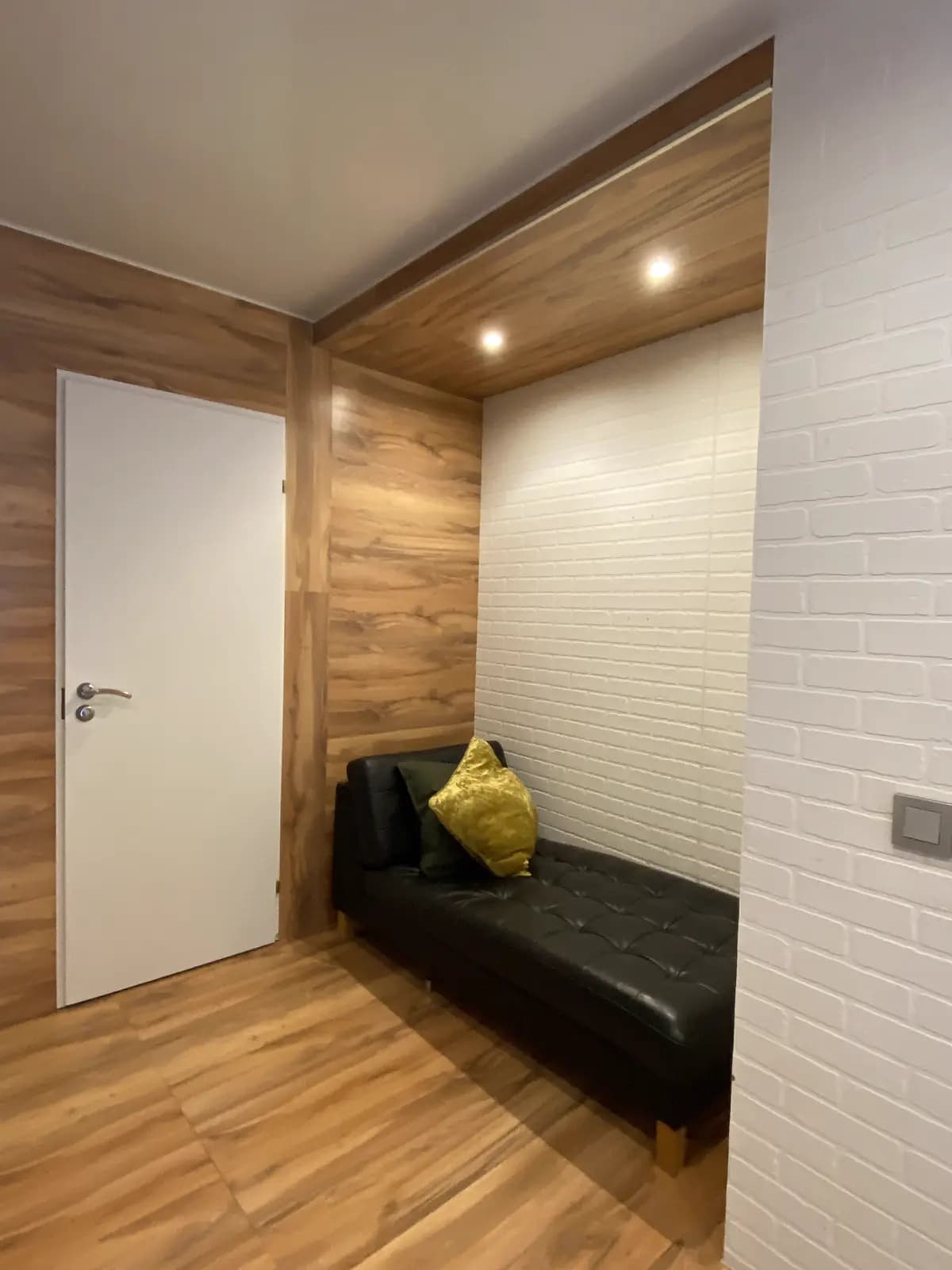 Reading nook with a black leather daybed set into a walnut frame against white brick texture
