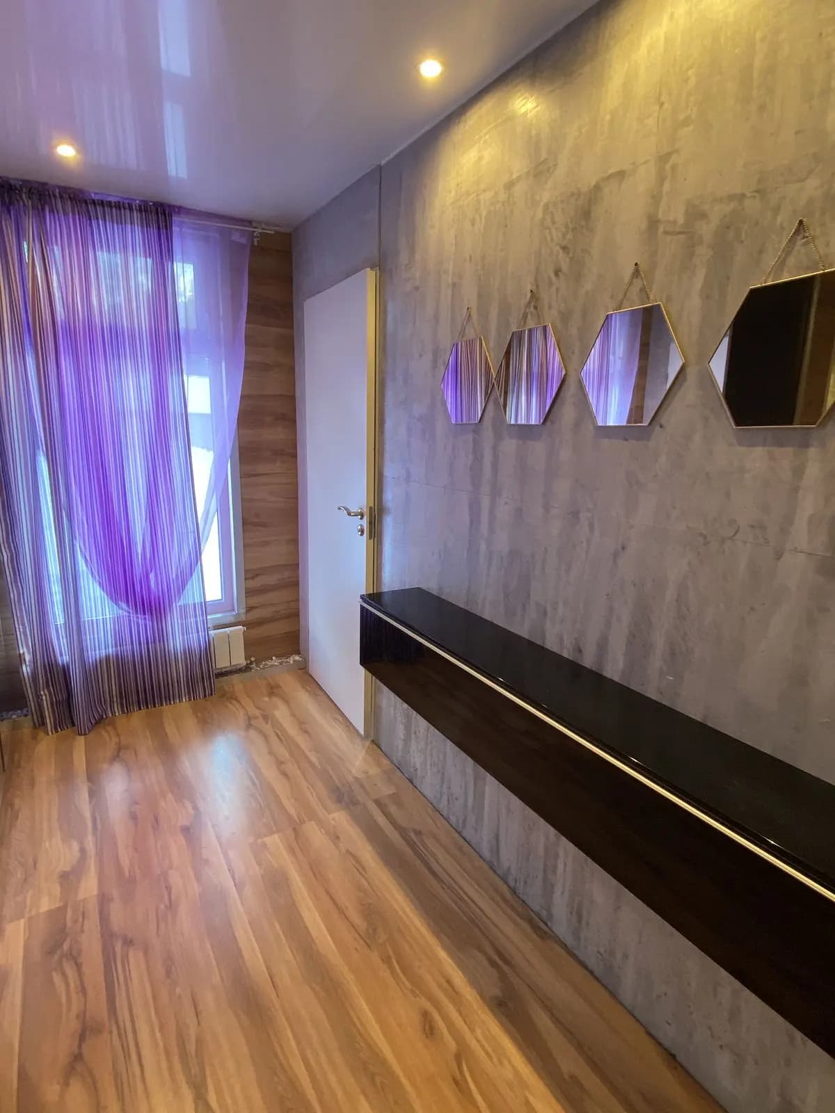 Concrete-texture feature wall with hexagonal mirrors, a floating black console, and sheer violet curtains