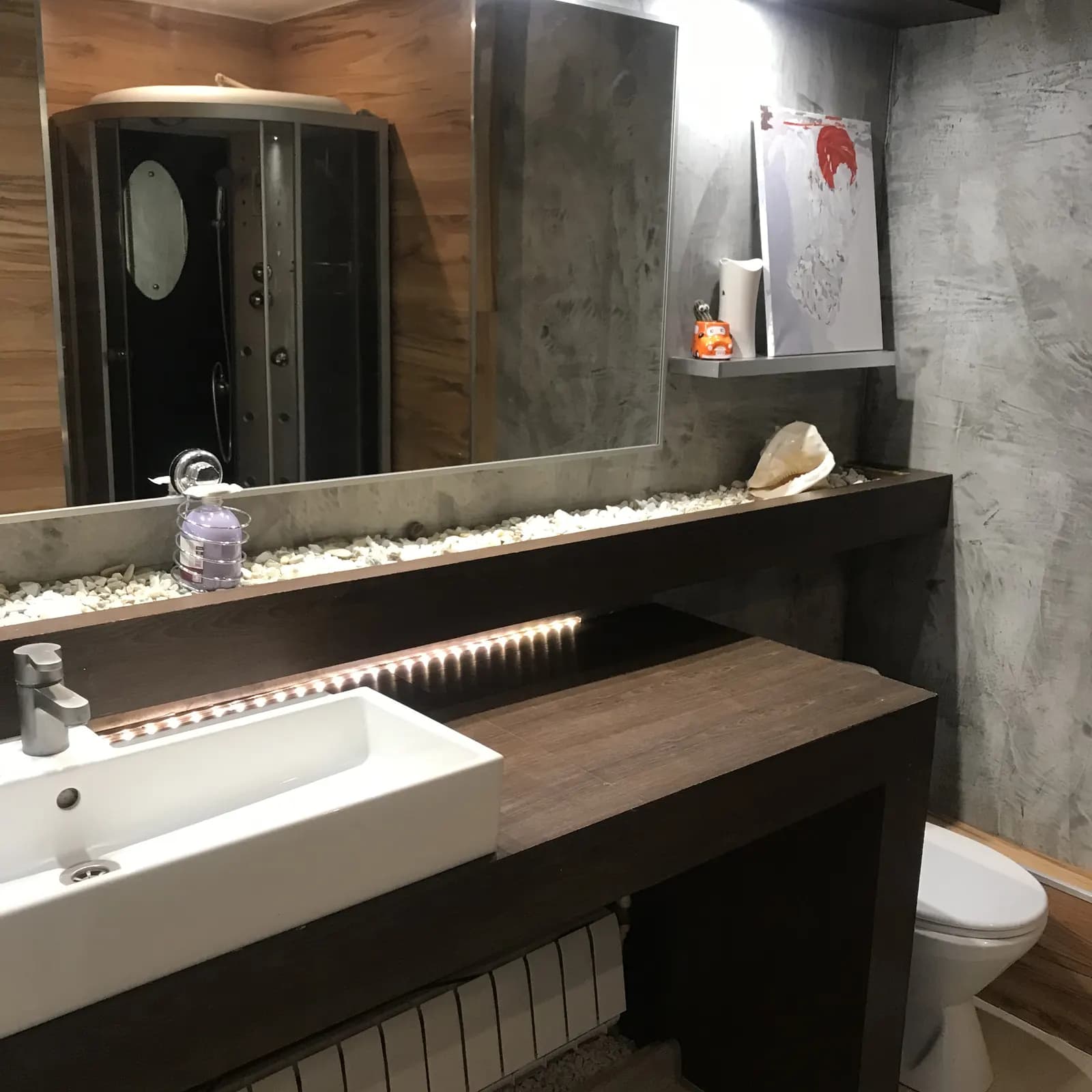Bathroom counter in dark wood with a white vessel sink and pebble-lined ledge