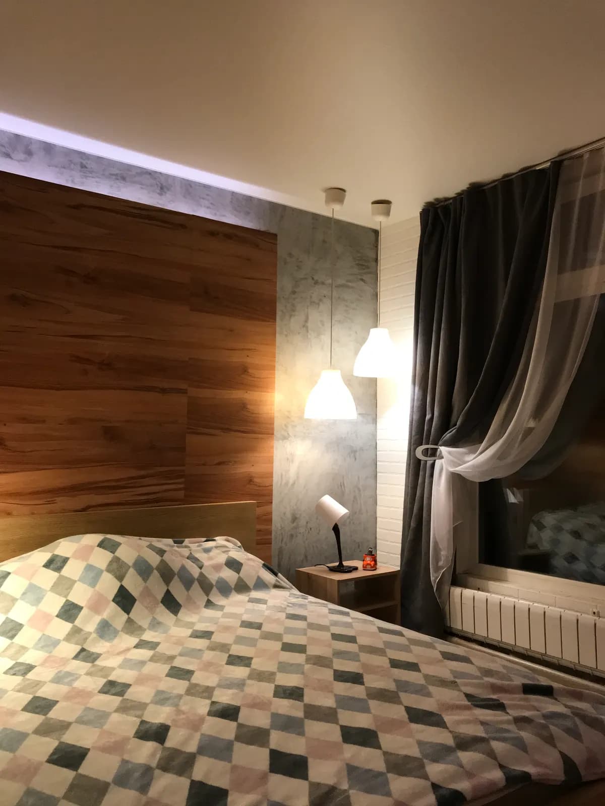 Bedroom with a walnut headboard wall, checkered quilt, and pendant reading lights