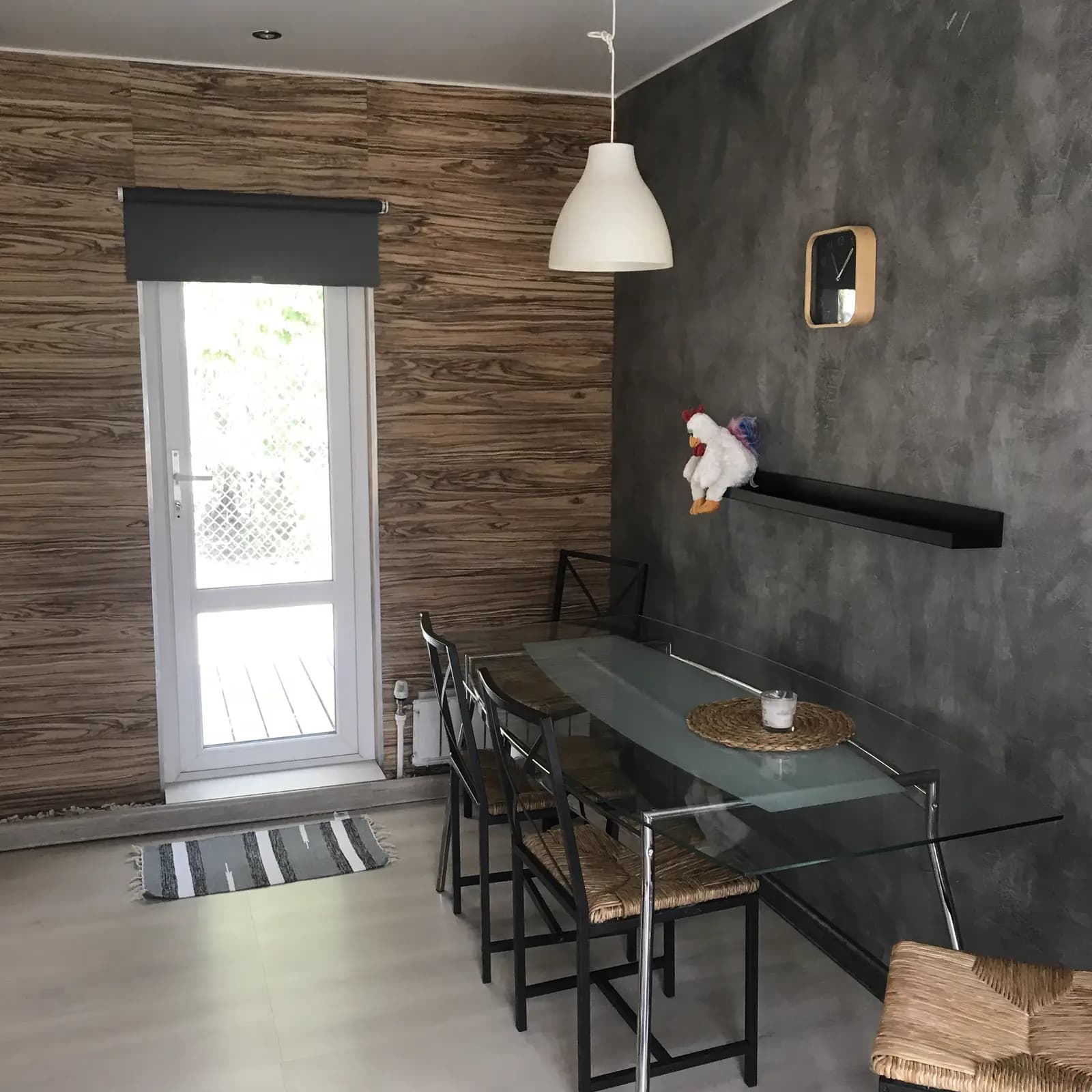 Glass dining table under a white pendant against a hand-finished grey plaster wall