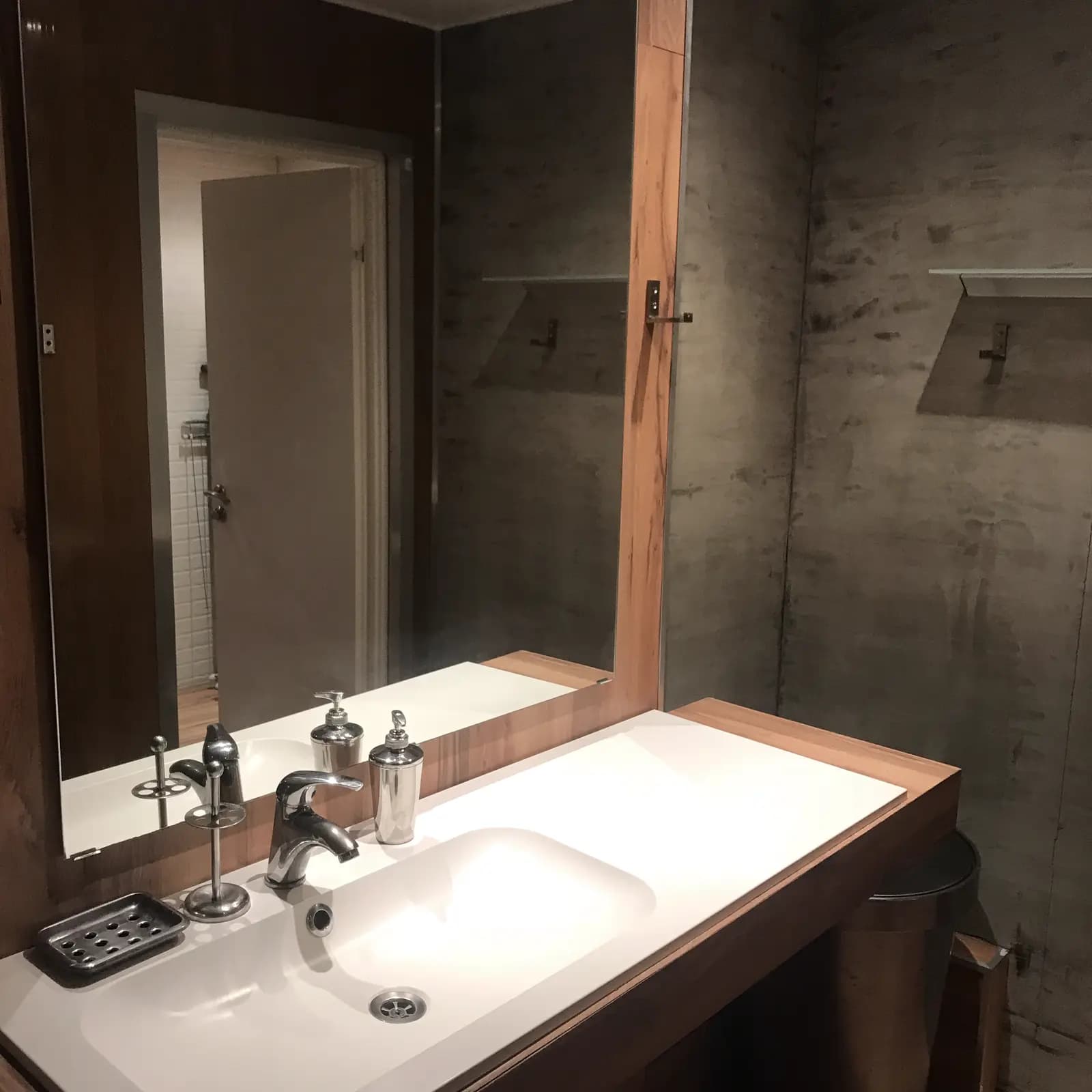 Bathroom vanity with a white counter, dark-framed mirror, and concrete-texture walls
