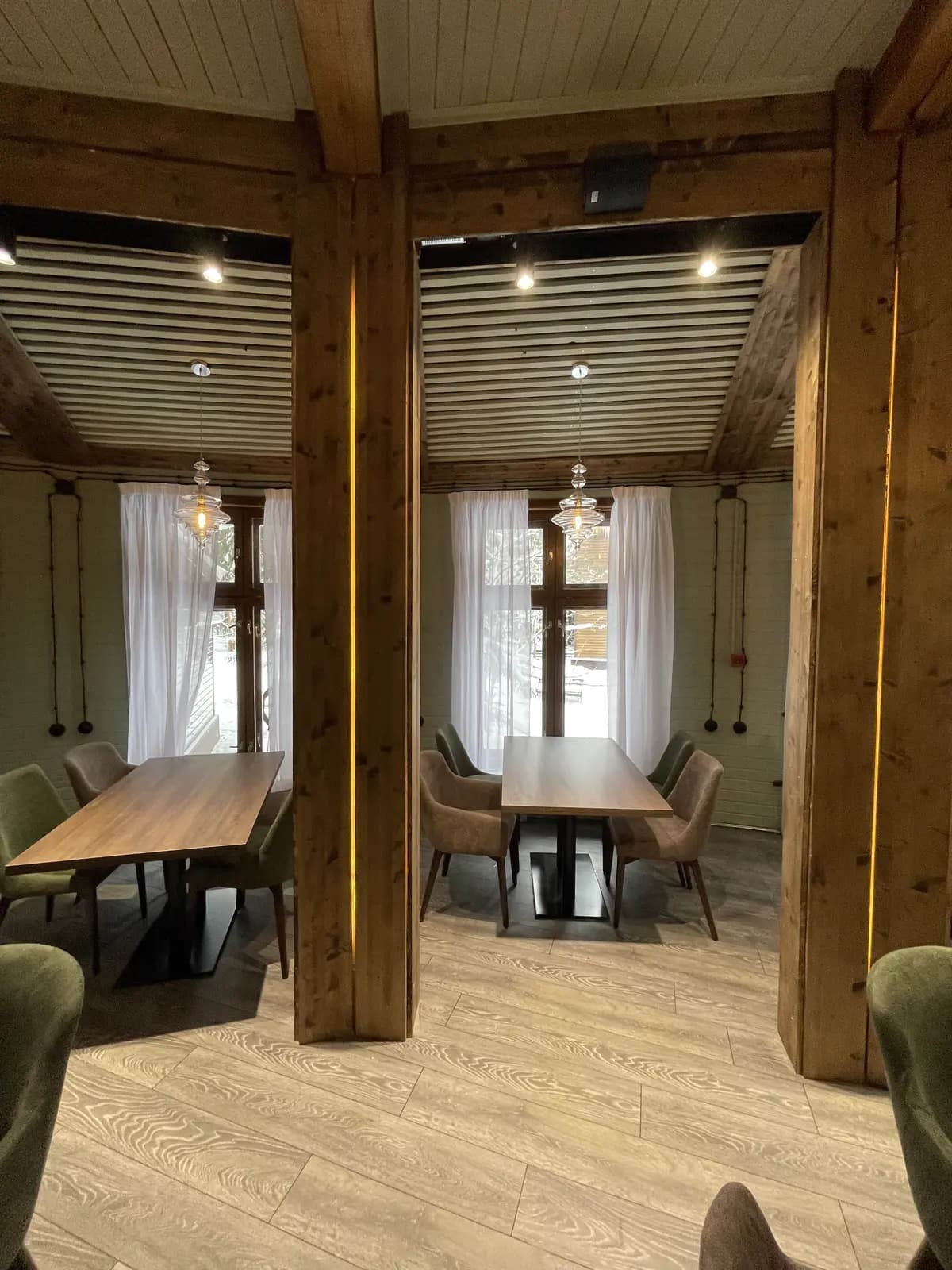 Dining tables set between original timber columns with brass-lit edges and sheer curtains