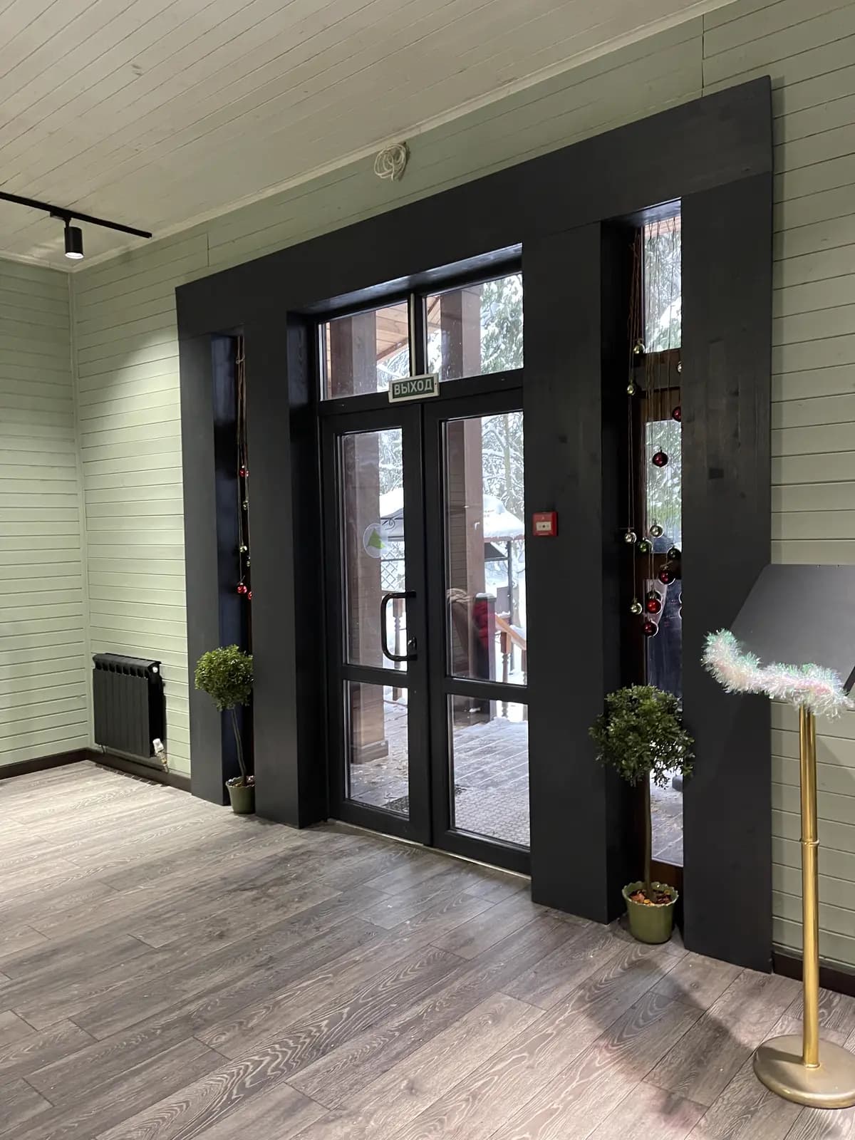 Restaurant entry with black-framed glass doors, pale plank walls, and potted greenery